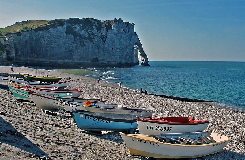 Bateaux de pêche colorés sur une plage de galets normande avec falaises en arrière-plan